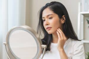 A woman looking in the mirror, considering PRP facial vs. microneedling