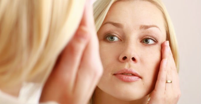 Woman examining her face in a mirror, related to Old Town Med Spa.