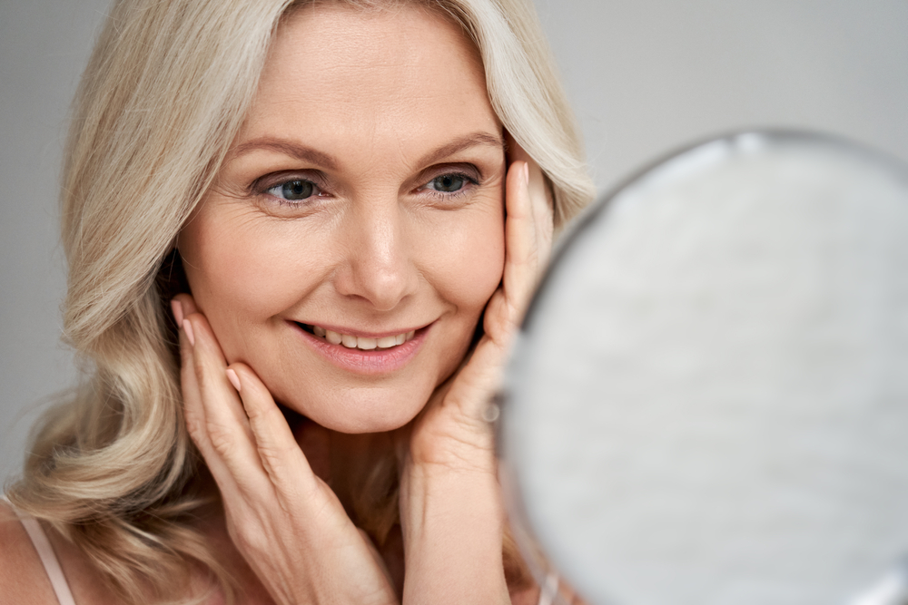 Woman smiling while looking in a mirror, related to exosome therapy.