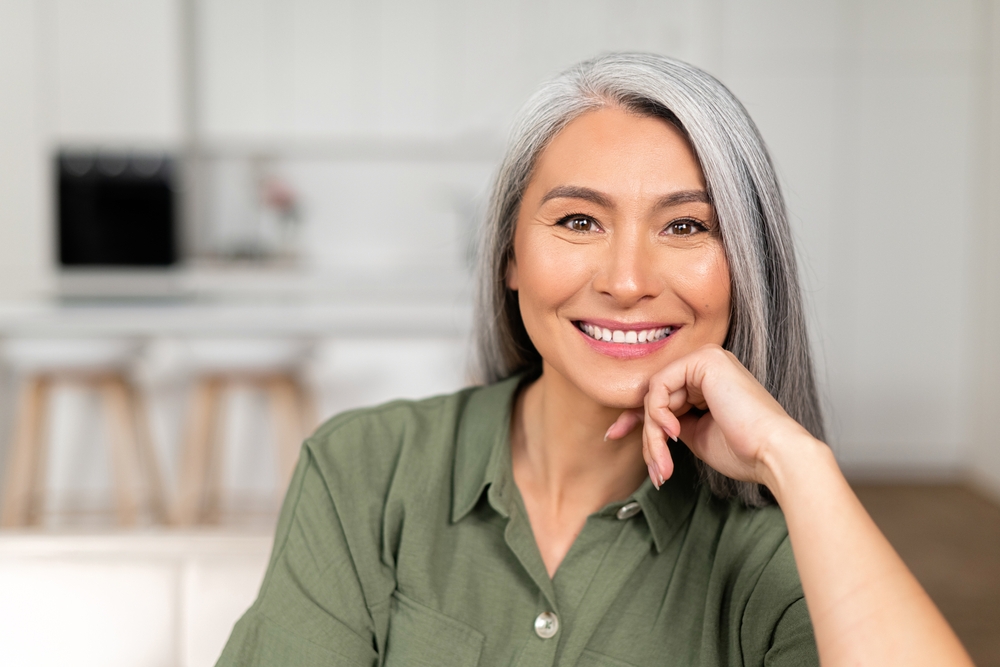 Smiling woman with gray hair in a green shirt, representing vitality and rejuvenation.